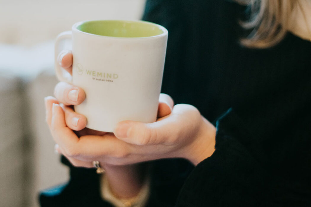 Kvinna håller i en mugg med texten WeMind