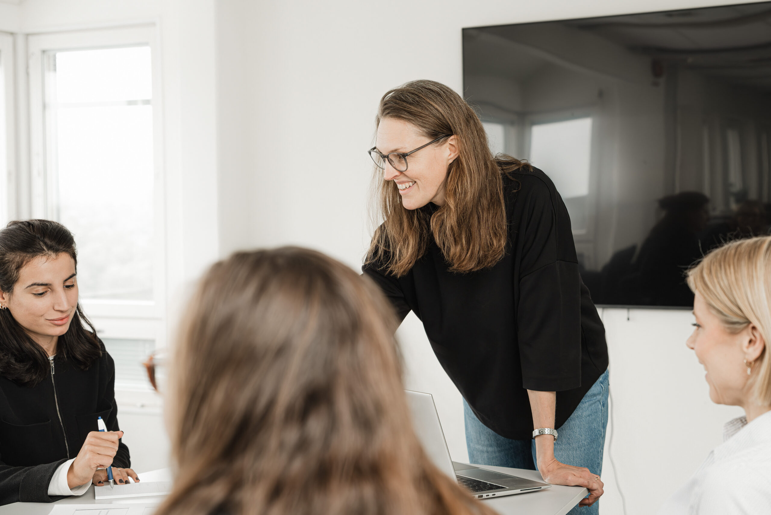 En person står lutad över ett bord i ett ljust rum med en stor svart skärm på väggen.